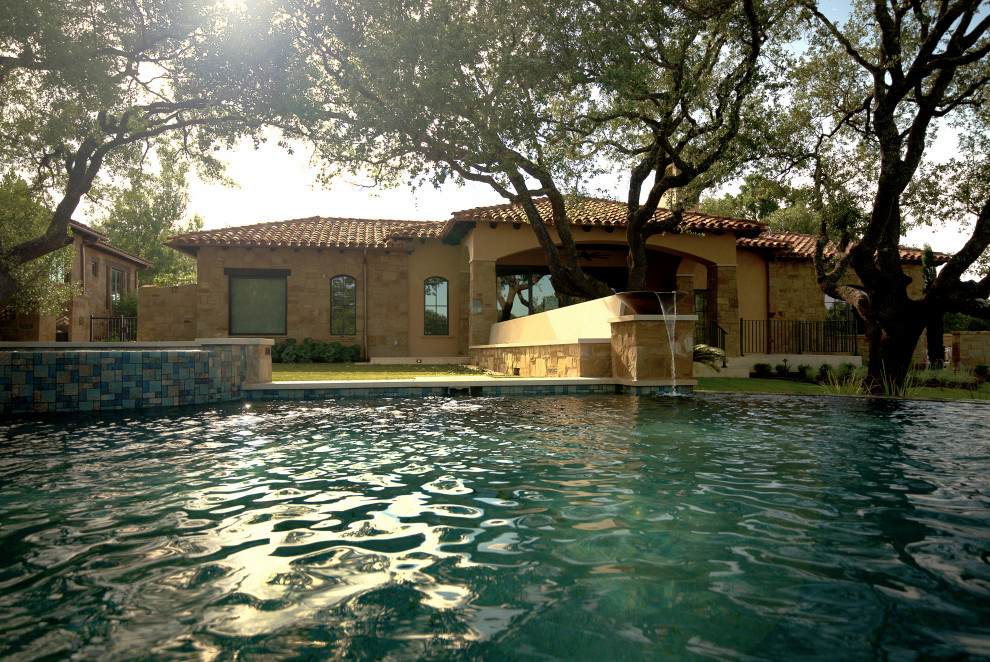 Ispirazione per una piscina a sfioro infinito mediterranea a "C" di medie dimensioni e dietro casa con fontane e pavimentazioni in pietra naturale