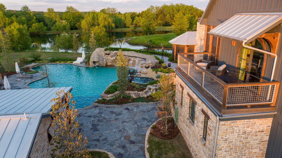 На фото: огромный естественный бассейн произвольной формы на заднем дворе в стиле кантри с перегородкой для приватности и покрытием из каменной брусчатки с