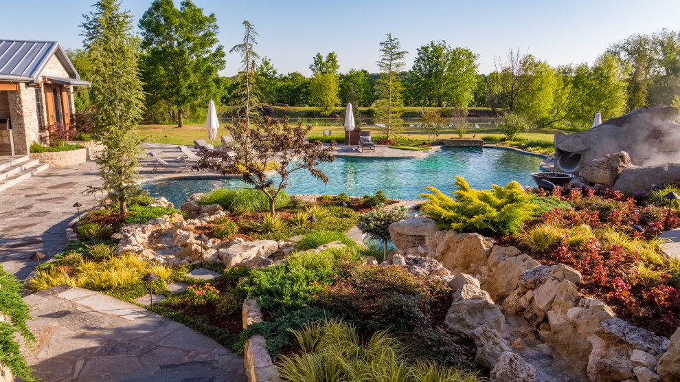 Inspiration for an expansive farmhouse back custom shaped natural swimming pool in Oklahoma City with with pool landscaping and natural stone paving.