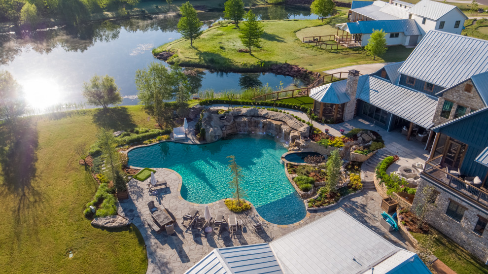 Ejemplo de piscina natural campestre extra grande a medida en patio trasero con paisajismo de piscina y adoquines de piedra natural