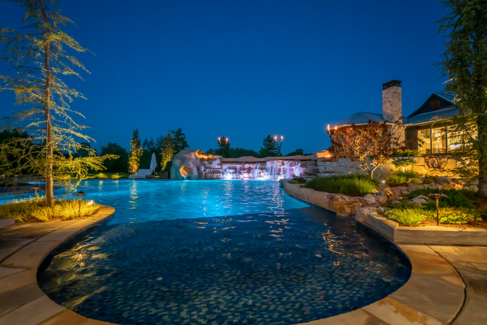 Ejemplo de piscina natural de estilo de casa de campo extra grande a medida en patio trasero con privacidad y adoquines de piedra natural
