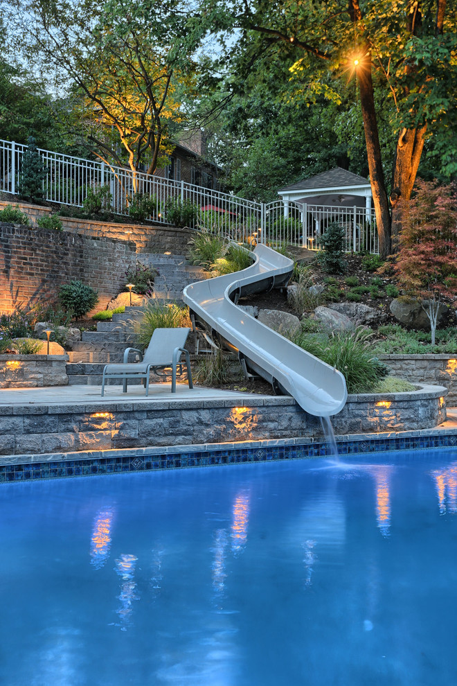 Diseño de piscina con tobogán moderna de tamaño medio rectangular en patio trasero con adoquines de hormigón