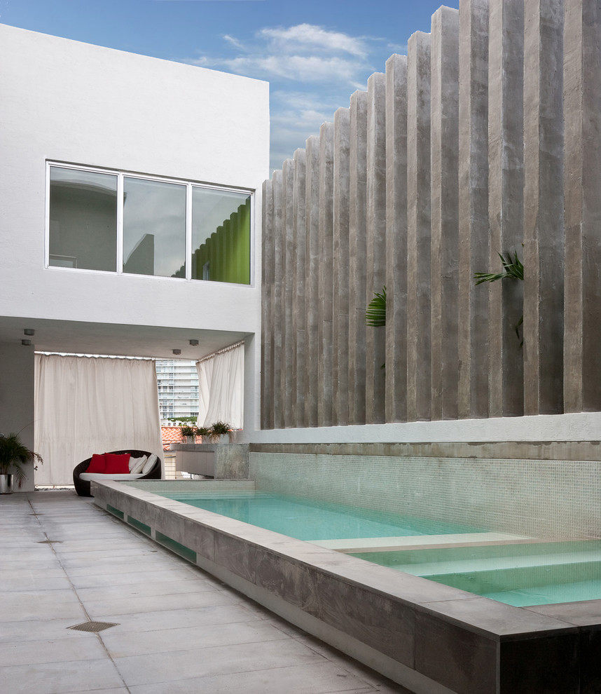 Idée de décoration pour une grande piscine à débordement et latérale minimaliste rectangle avec un bain bouillonnant et des pavés en béton.
