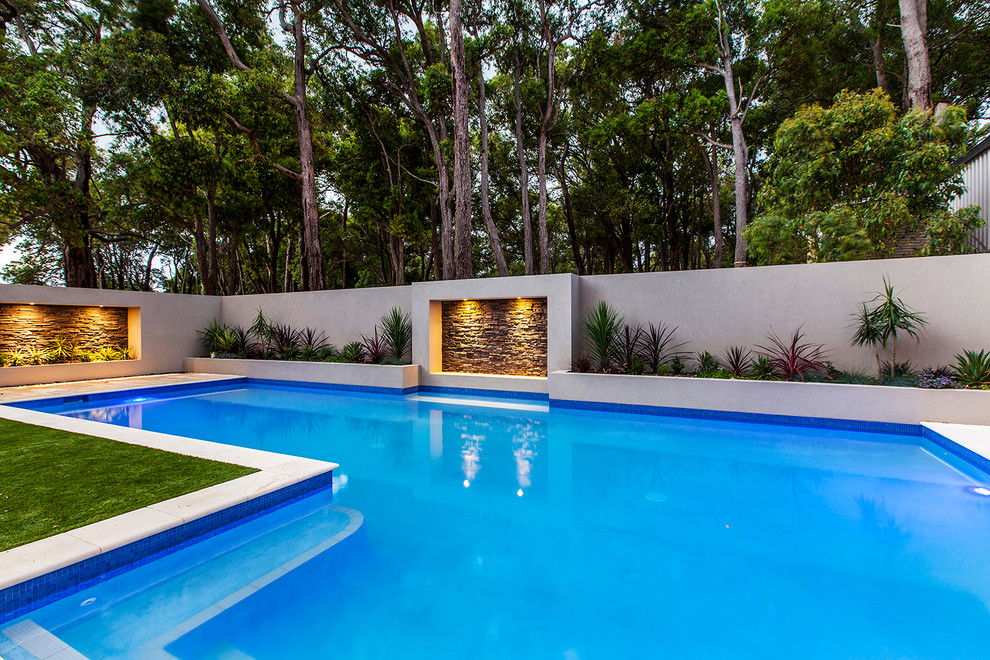 Imagen de piscina con fuente alargada contemporánea grande en forma de L en patio trasero con losas de hormigón