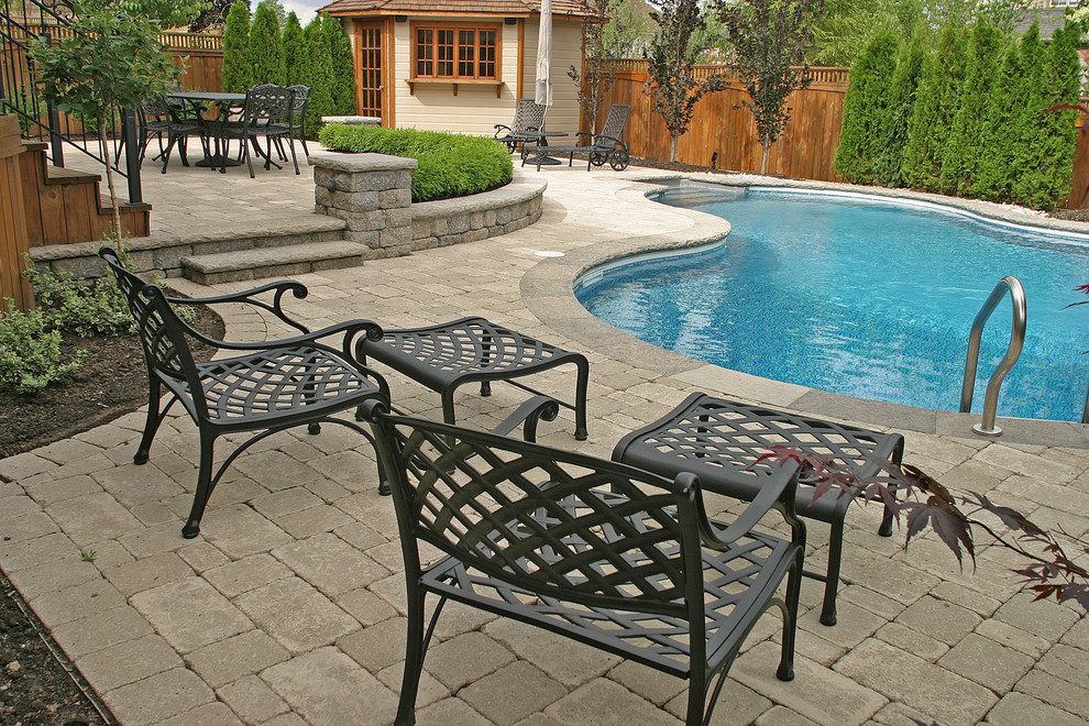Modelo de casa de la piscina y piscina alargada tradicional renovada de tamaño medio tipo riñón en patio trasero con adoquines de hormigón