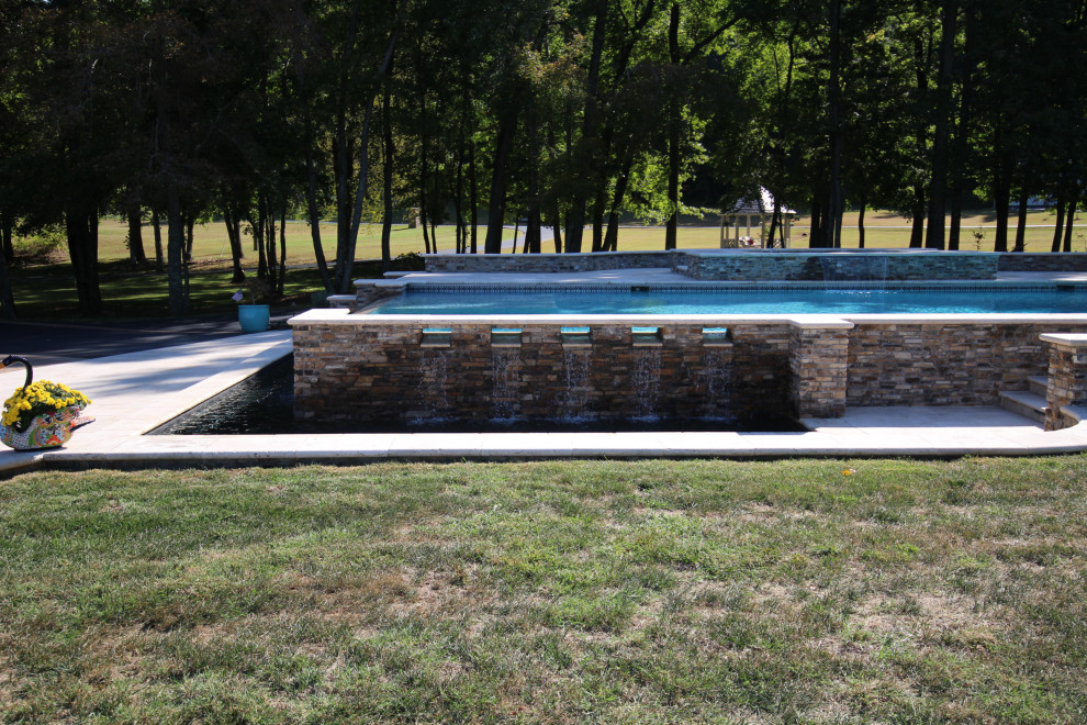 Foto de piscinas y jacuzzis infinitos clásicos grandes rectangulares en patio trasero con adoquines de piedra natural