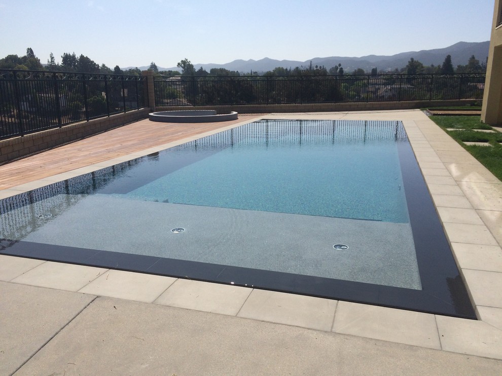 Réalisation d'une grande piscine à débordement et arrière design rectangle avec une dalle de béton.