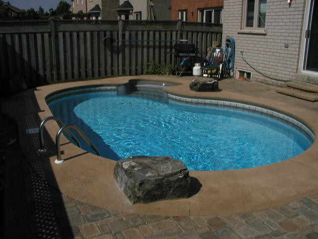 Foto de piscina natural clásica pequeña tipo riñón en patio trasero con suelo de hormigón estampado