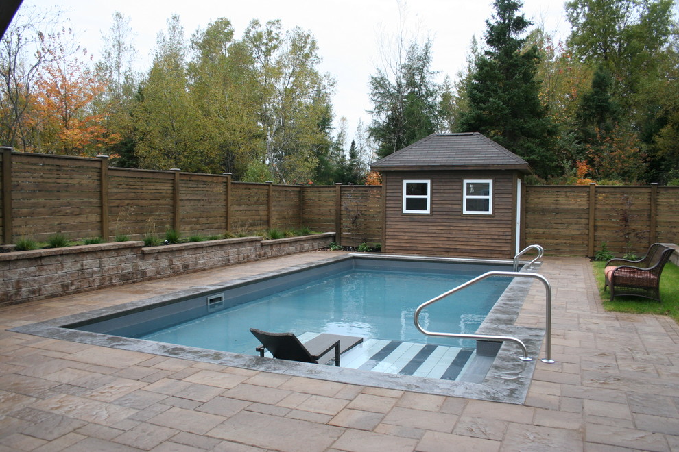 Diseño de piscina tradicional de tamaño medio rectangular en patio trasero con adoquines de hormigón