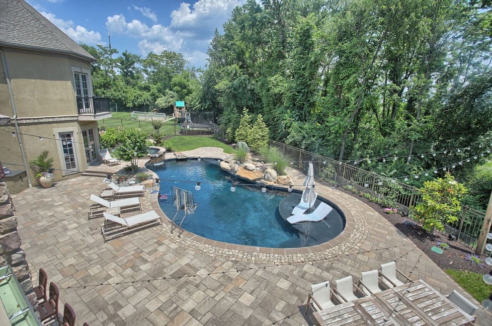 Exemple d'une grande piscine arrière tendance en forme de haricot avec un bain bouillonnant et des pavés en béton.