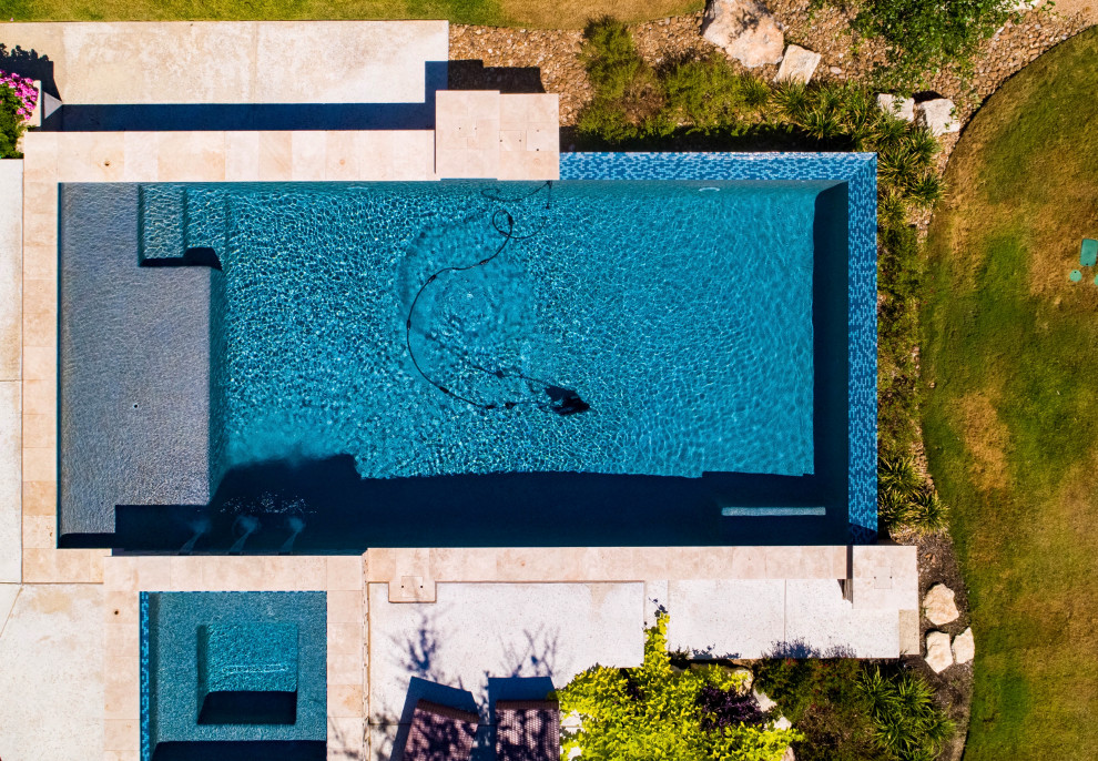 Esempio di una grande piscina a sfioro infinito moderna rettangolare dietro casa con paesaggistica bordo piscina e lastre di cemento