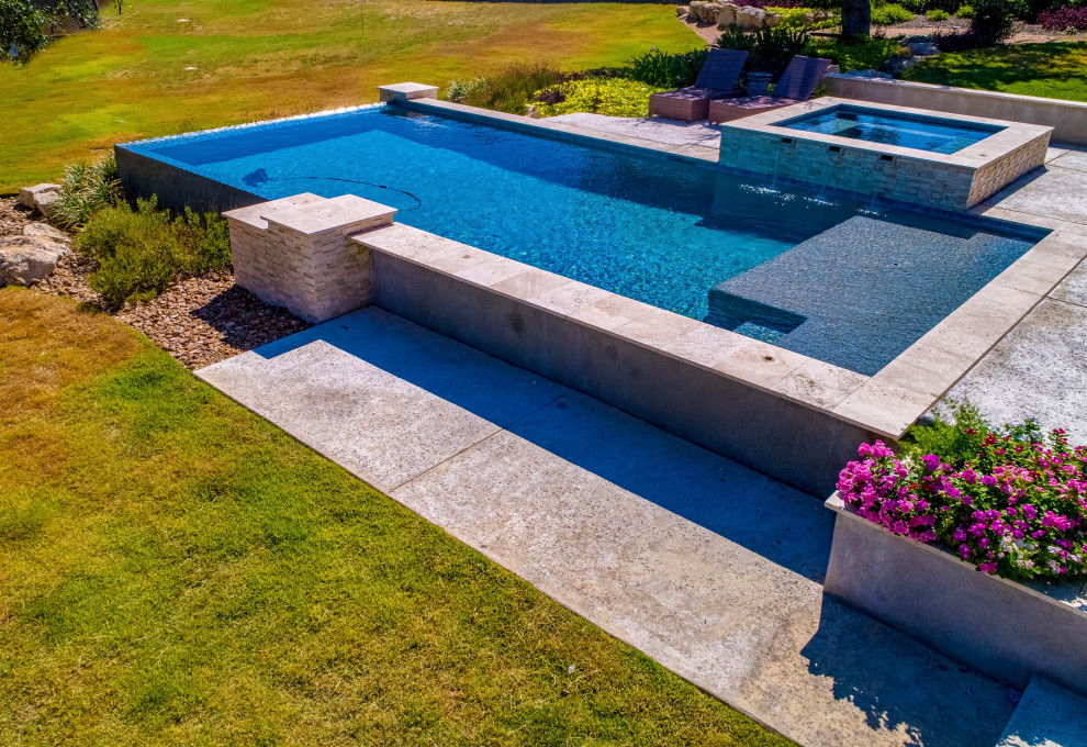 Immagine di una grande piscina a sfioro infinito minimalista rettangolare dietro casa con paesaggistica bordo piscina e lastre di cemento