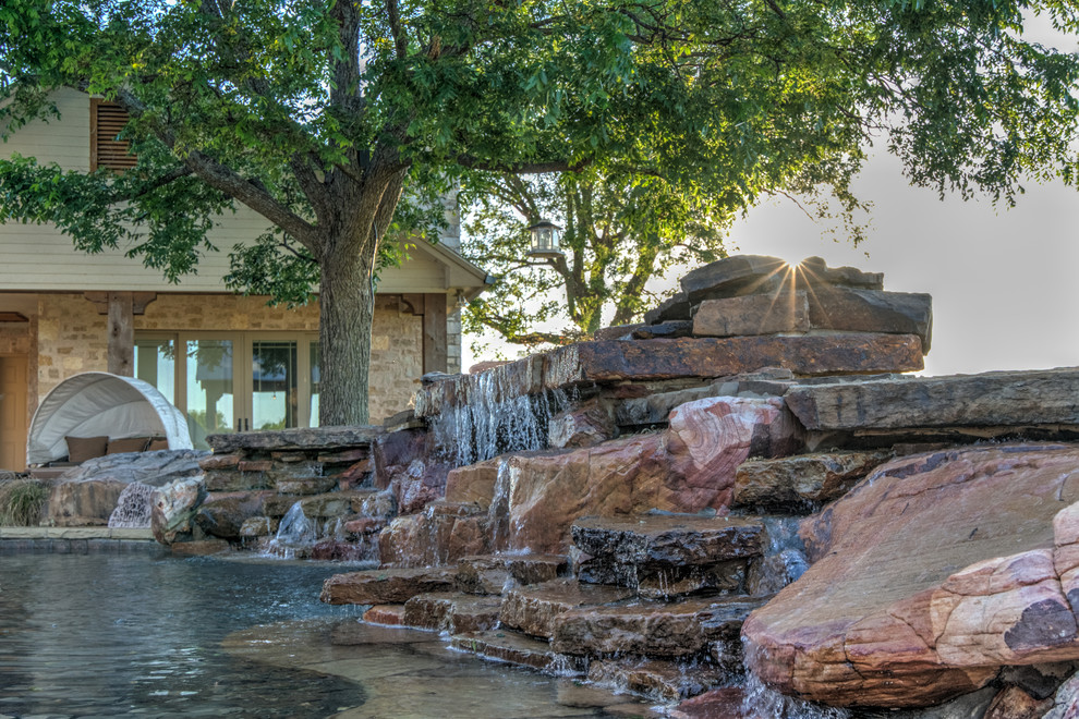 Esempio di un'ampia piscina naturale tropicale personalizzata dietro casa con una vasca idromassaggio e pavimentazioni in pietra naturale