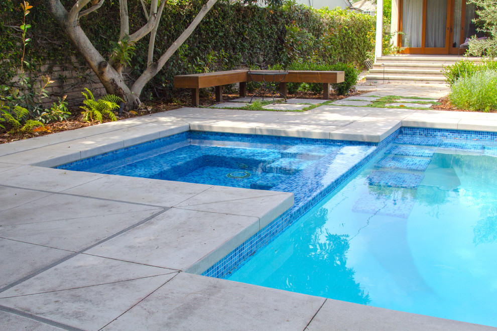 Modelo de piscinas y jacuzzis alargados actuales de tamaño medio rectangulares en patio trasero con losas de hormigón