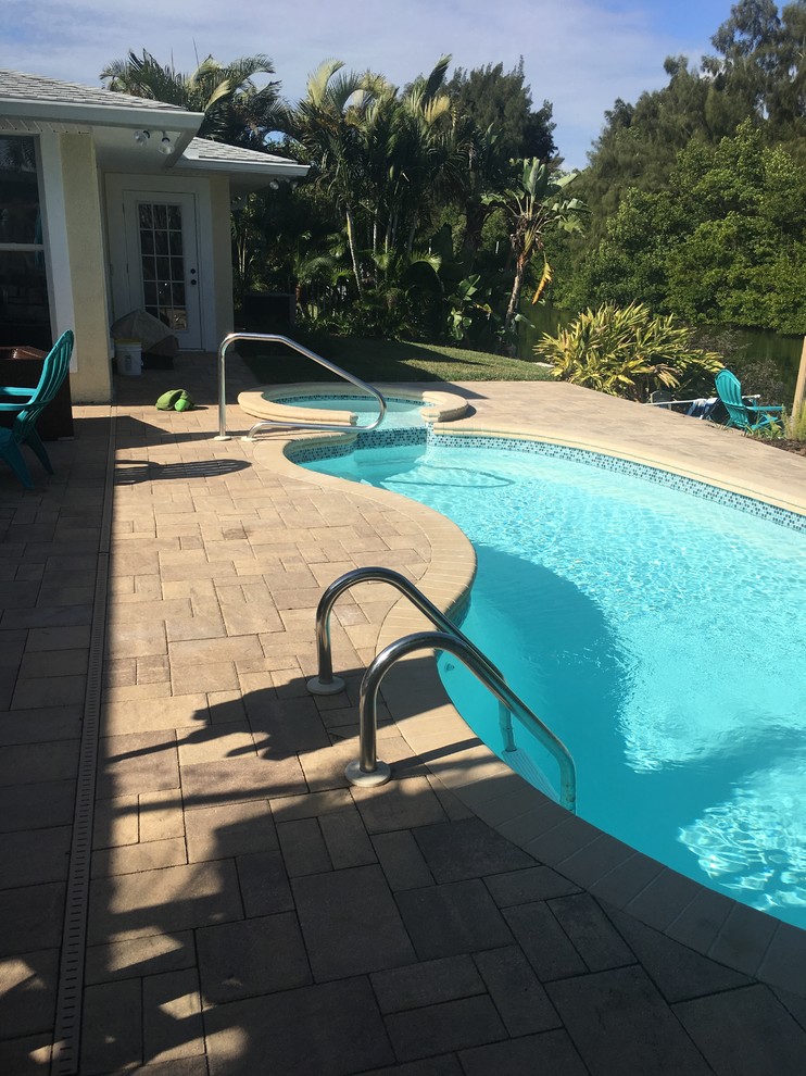 Imagen de piscinas y jacuzzis alargados tropicales pequeños tipo riñón en patio trasero con adoquines de ladrillo