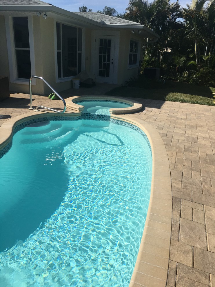 Immagine di una piccola piscina monocorsia tropicale a "C" dietro casa con una vasca idromassaggio e pavimentazioni in mattoni