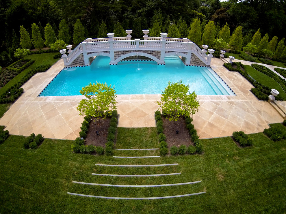 На фото: огромный прямоугольный бассейн на заднем дворе в классическом стиле с фонтаном и настилом с
