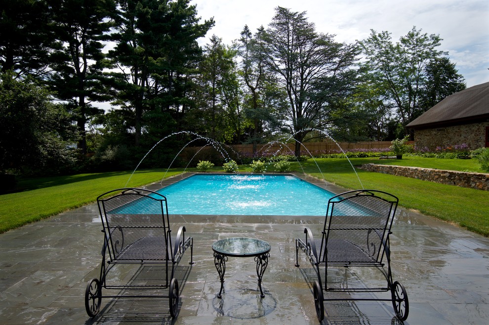 Ejemplo de piscina con fuente alargada clásica de tamaño medio rectangular en patio trasero con adoquines de piedra natural