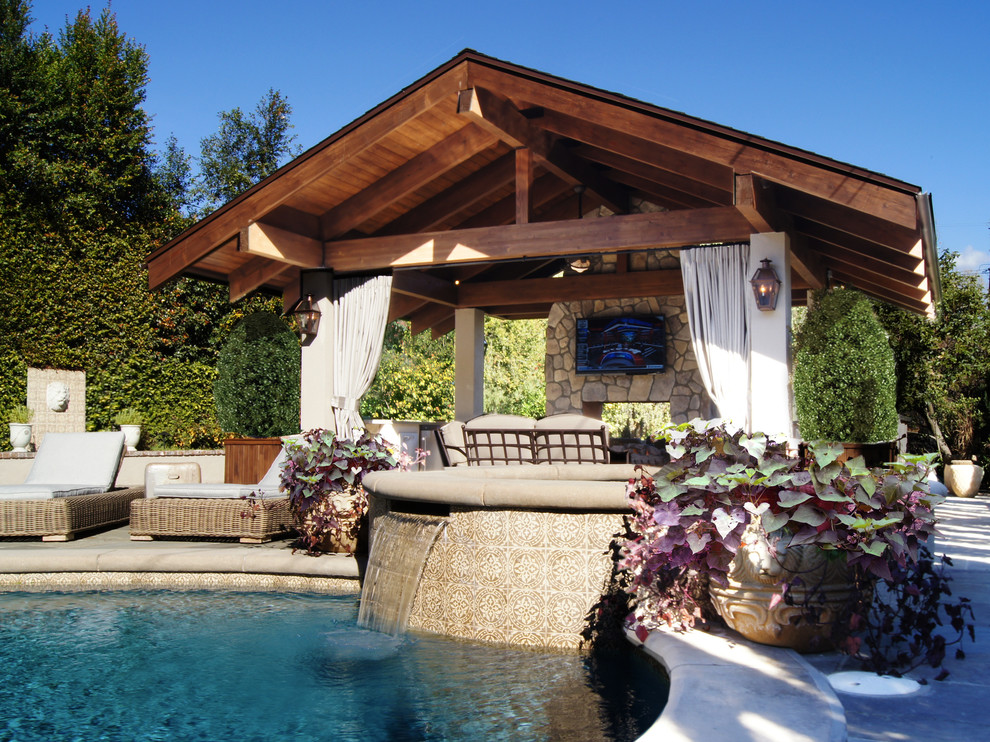 Modelo de piscinas y jacuzzis naturales clásicos de tamaño medio en patio trasero con adoquines de hormigón