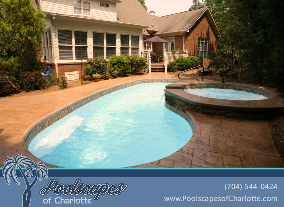 Immagine di una grande piscina chic a "C" dietro casa con una vasca idromassaggio e cemento stampato