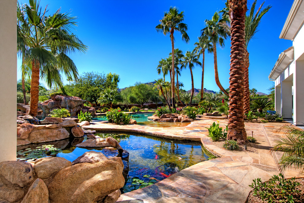 Immagine di un'ampia piscina tropicale personalizzata dietro casa con fontane e pavimentazioni in pietra naturale