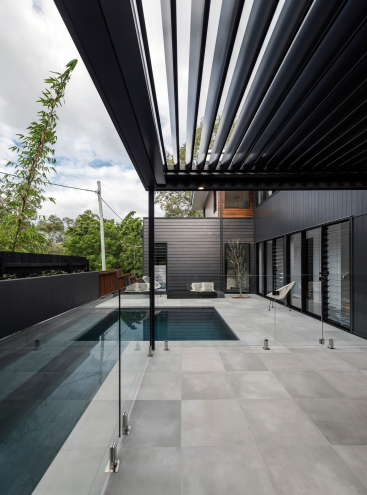 Modelo de piscina alargada contemporánea en patio lateral con suelo de baldosas