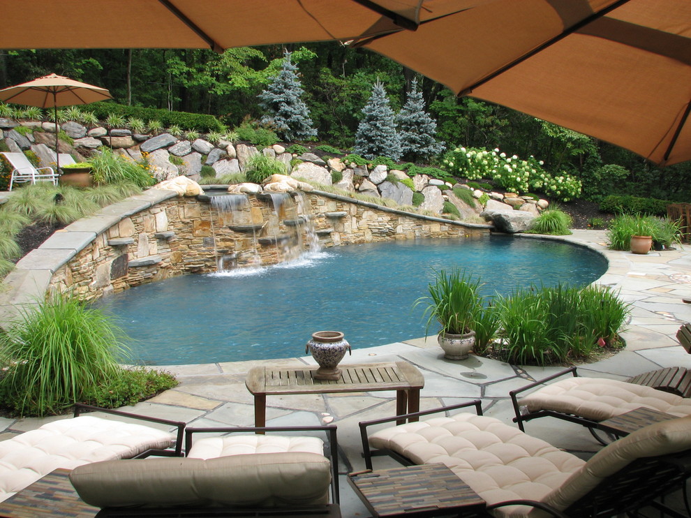 Diseño de piscinas y jacuzzis alargados de estilo americano grandes redondeados en patio trasero con adoquines de piedra natural