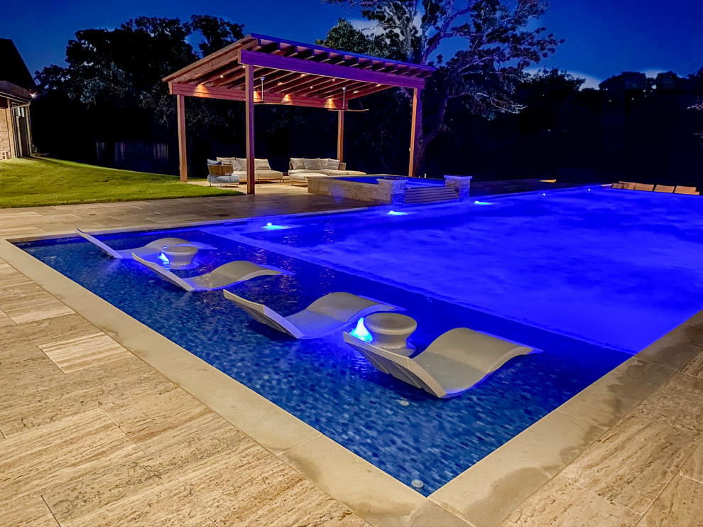 Стильный дизайн: огромный прямоугольный бассейн-инфинити на заднем дворе в стиле неоклассика (современная классика) с фонтаном и покрытием из каменной брусчатки - последний тренд