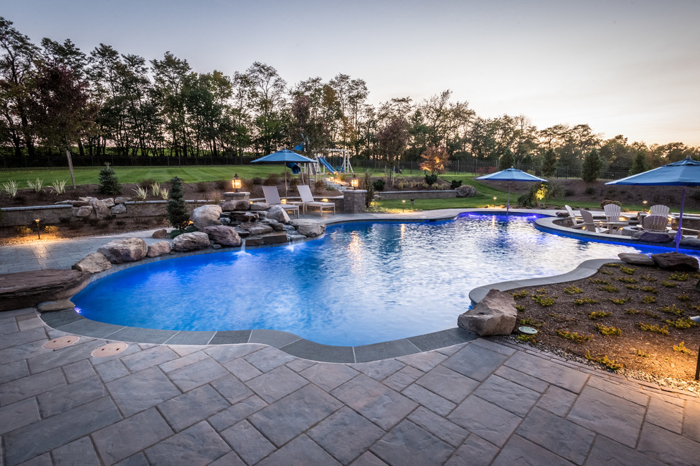 Diseño de piscina natural tradicional renovada grande a medida en patio trasero con adoquines de hormigón