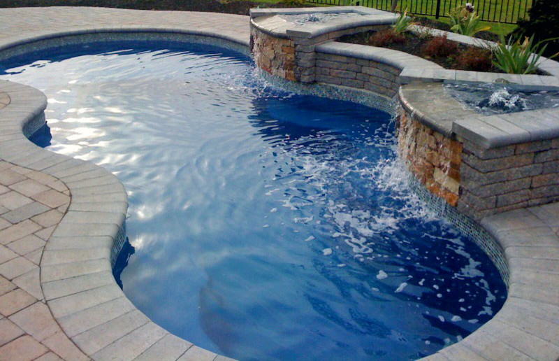 Ejemplo de piscina con fuente actual de tamaño medio tipo riñón en patio trasero con adoquines de ladrillo