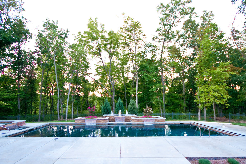 Diseño de piscina con fuente industrial extra grande rectangular en patio trasero con losas de hormigón