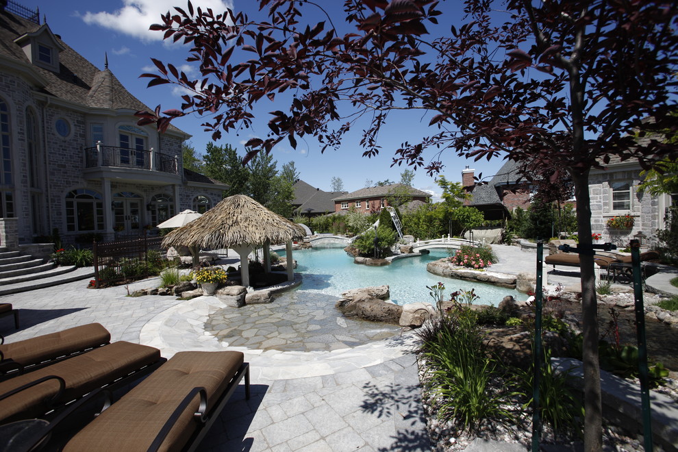 На фото: большой естественный бассейн на заднем дворе в средиземноморском стиле с водной горкой и покрытием из каменной брусчатки