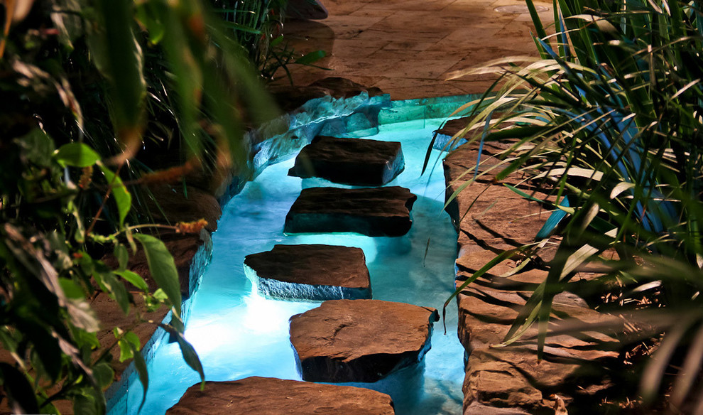 Ispirazione per una grande piscina naturale tropicale rettangolare dietro casa con pavimentazioni in pietra naturale e una dépendance a bordo piscina