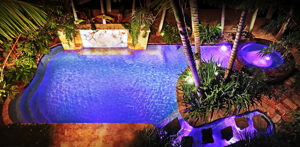 Idee per una grande piscina naturale tropicale rettangolare dietro casa con pavimentazioni in pietra naturale e una dépendance a bordo piscina
