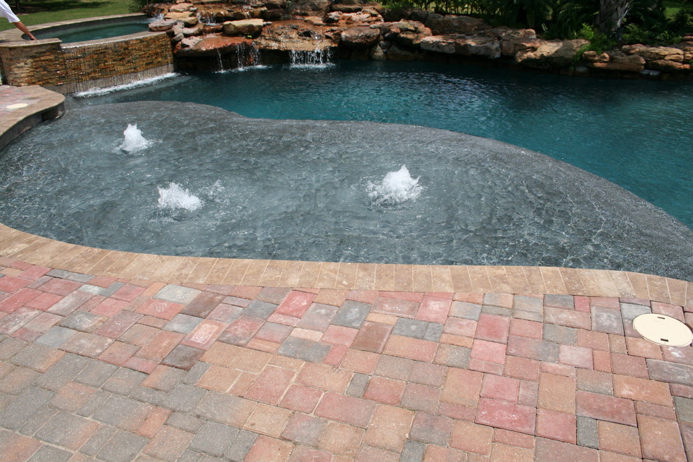 Diseño de piscinas y jacuzzis naturales tropicales grandes a medida en patio trasero con adoquines de ladrillo