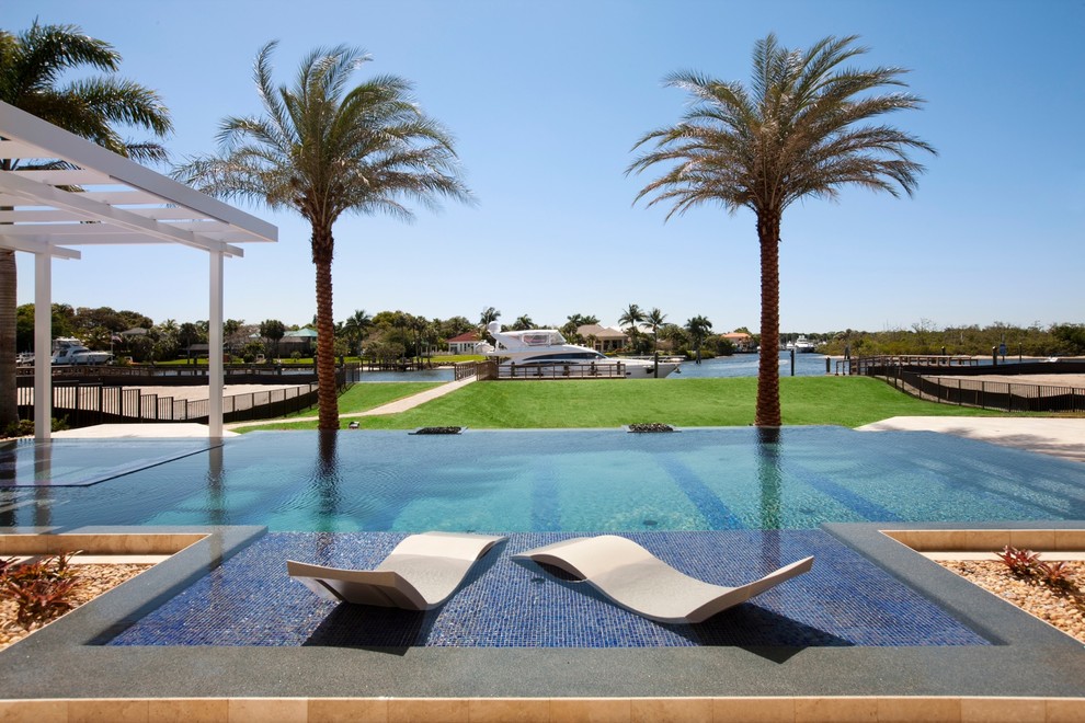 Foto de piscina infinita exótica extra grande rectangular en patio trasero con suelo de baldosas