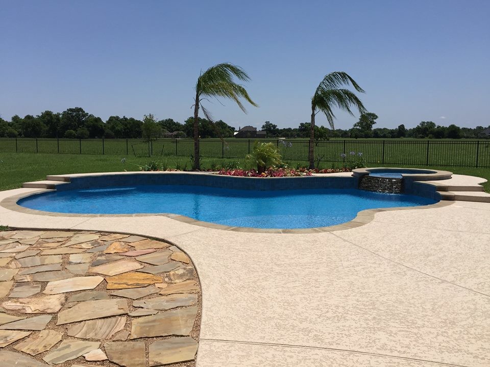 Idee per una grande piscina naturale tropicale personalizzata dietro casa con una vasca idromassaggio e lastre di cemento