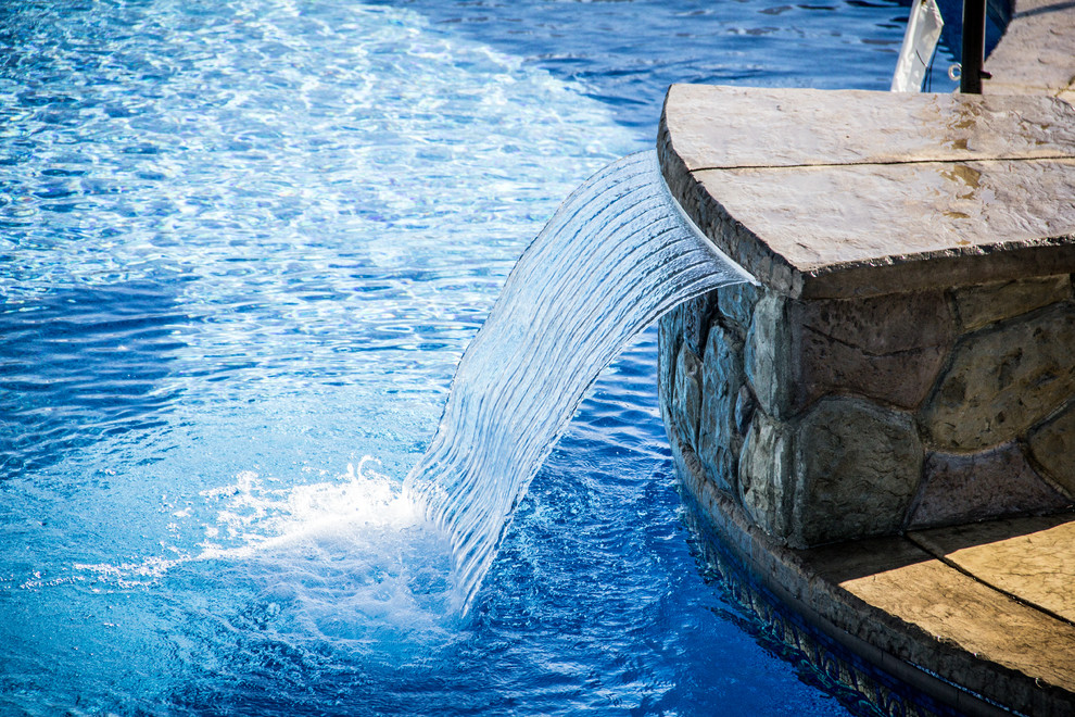 Modelo de piscina con fuente mediterránea grande a medida en patio trasero con suelo de hormigón estampado