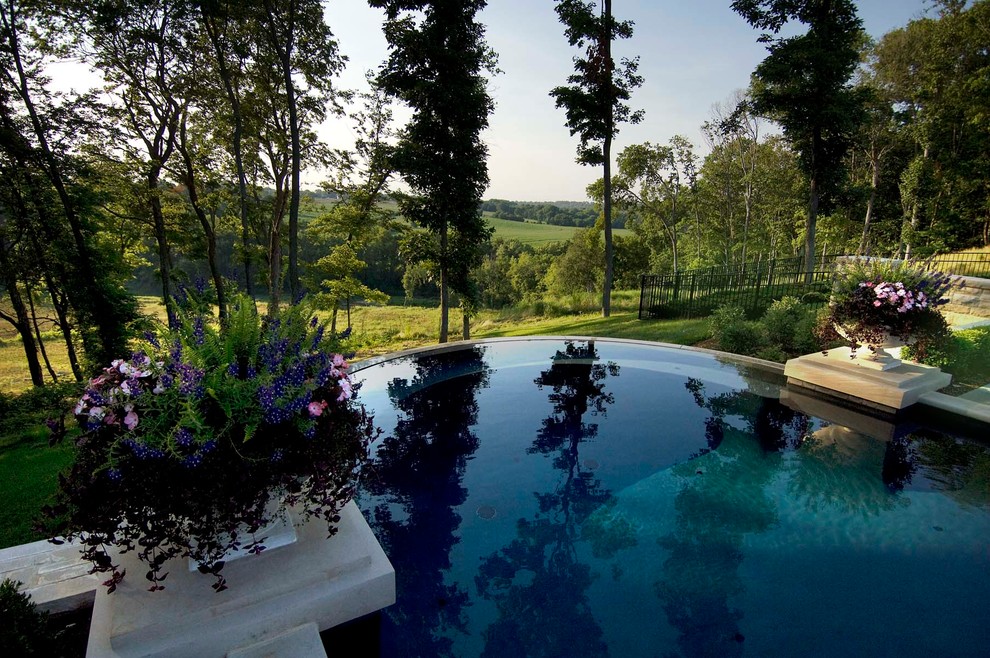 Diseño de piscina infinita clásica grande redondeada en patio trasero con adoquines de piedra natural