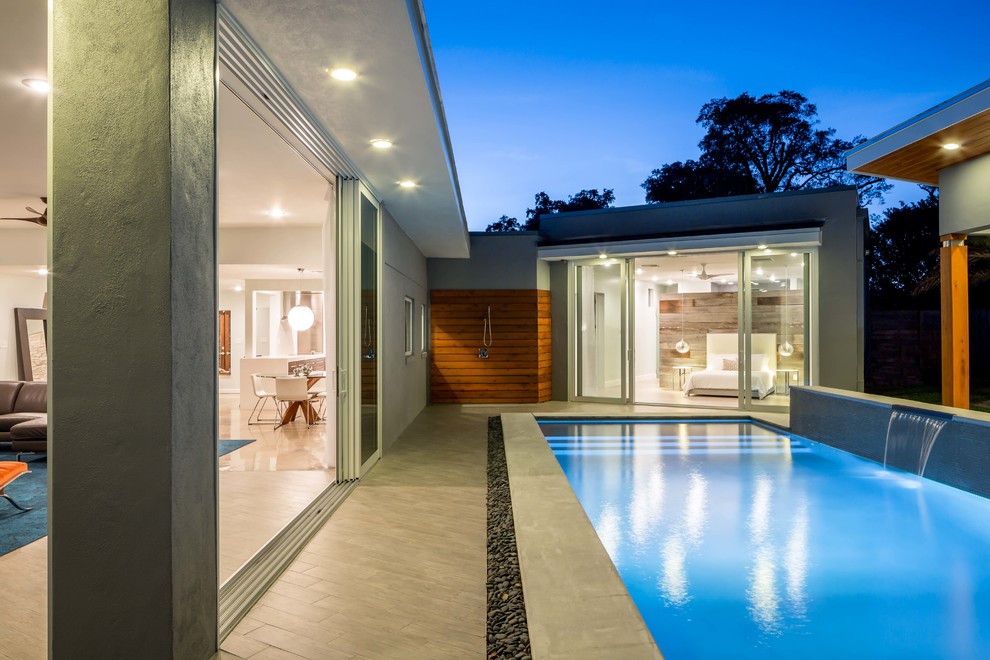 Esempio di una piscina minimalista rettangolare di medie dimensioni e dietro casa con fontane e piastrelle