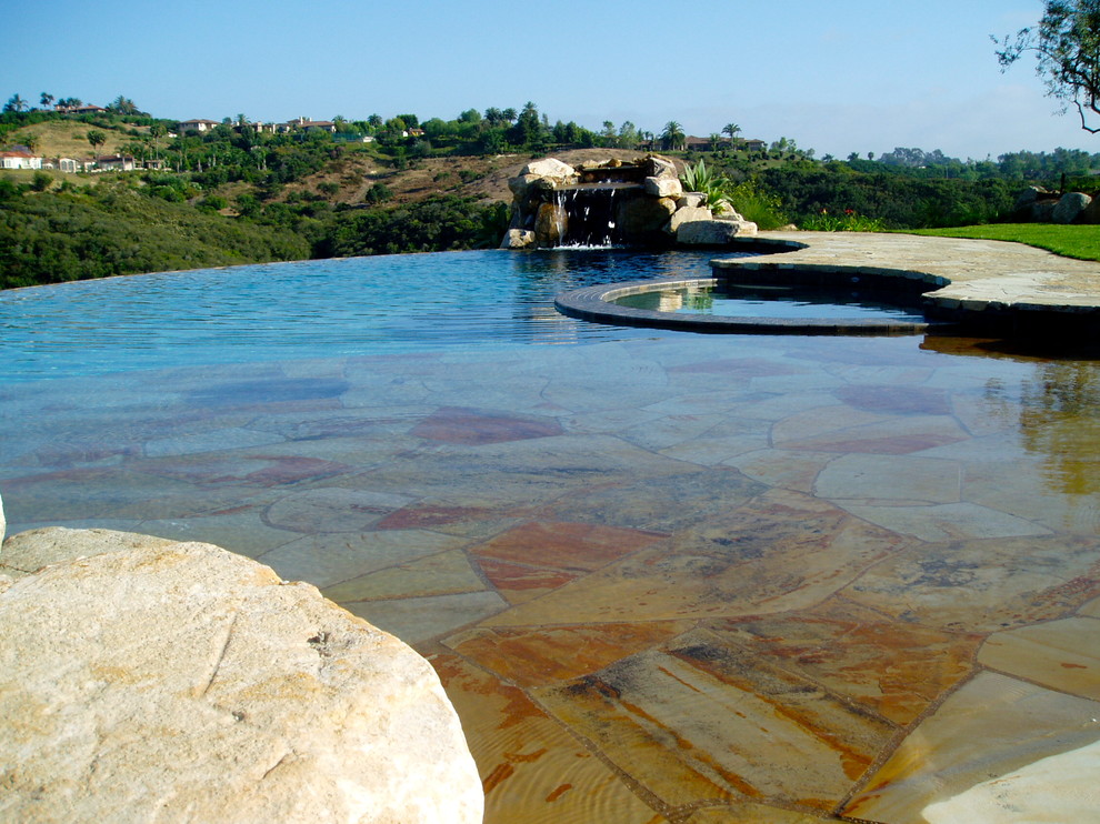 Tuscan backyard concrete paver and custom-shaped infinity hot tub photo in San Diego