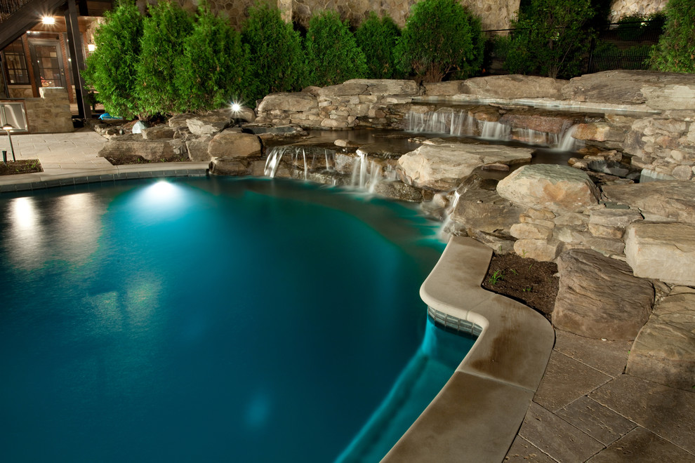 Ejemplo de piscina con fuente bohemia grande a medida en patio trasero con adoquines de piedra natural