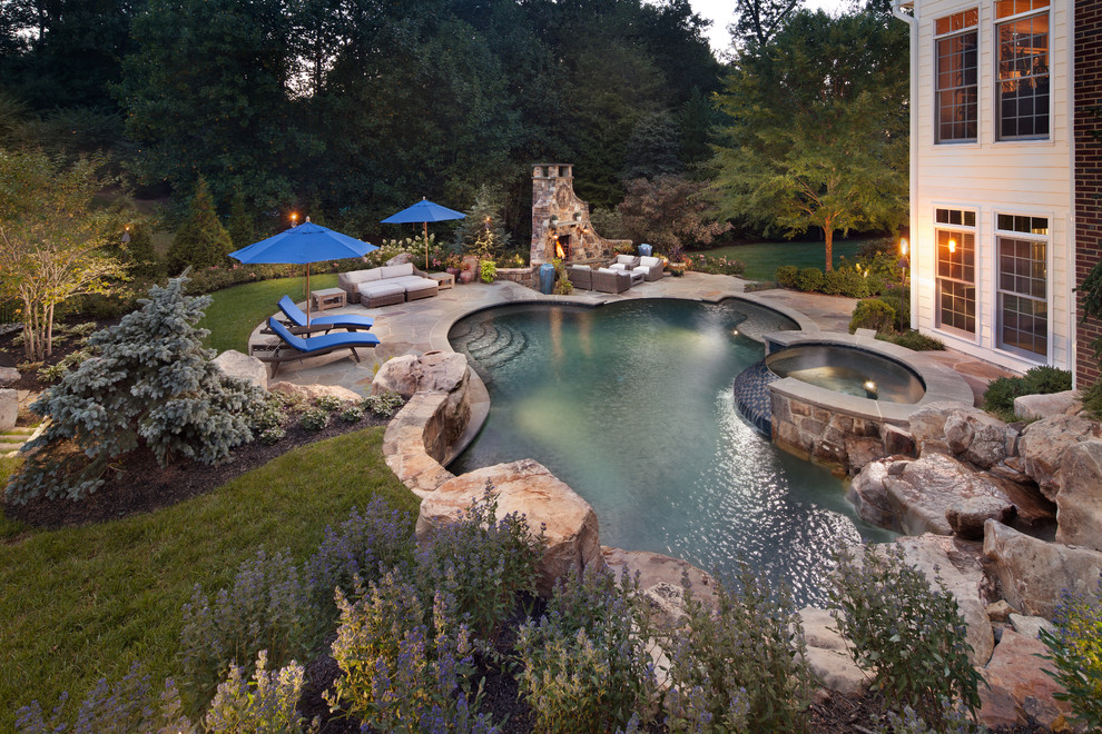 Immagine di una grande piscina tradizionale personalizzata dietro casa con pavimentazioni in pietra naturale e una vasca idromassaggio