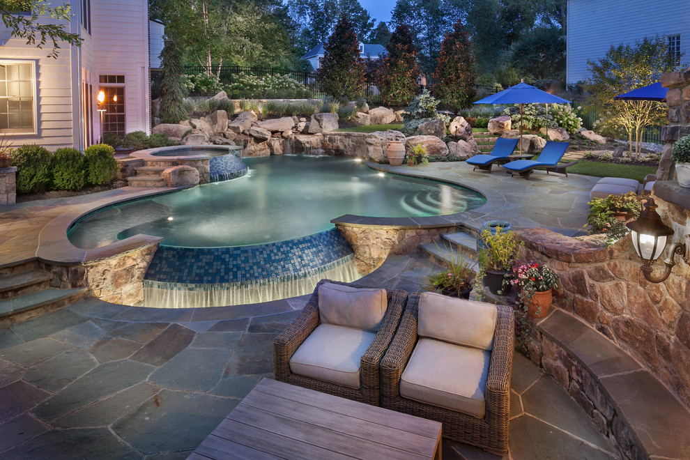 Exempel på en stor klassisk anpassad pool på baksidan av huset, med naturstensplattor och spabad