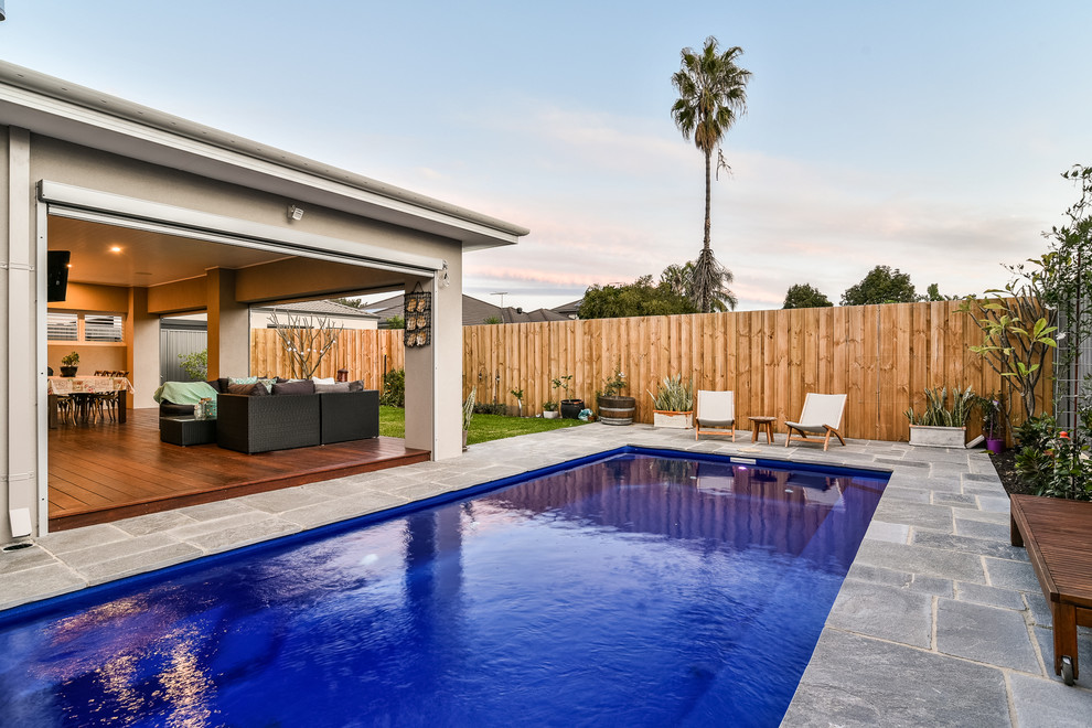 Diseño de piscina alargada moderna de tamaño medio rectangular en patio trasero con adoquines de piedra natural