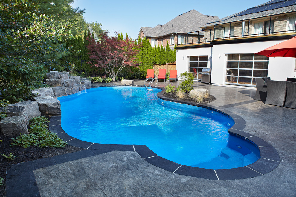 Пример оригинального дизайна: большой естественный бассейн произвольной формы на заднем дворе в современном стиле с фонтаном и покрытием из декоративного бетона