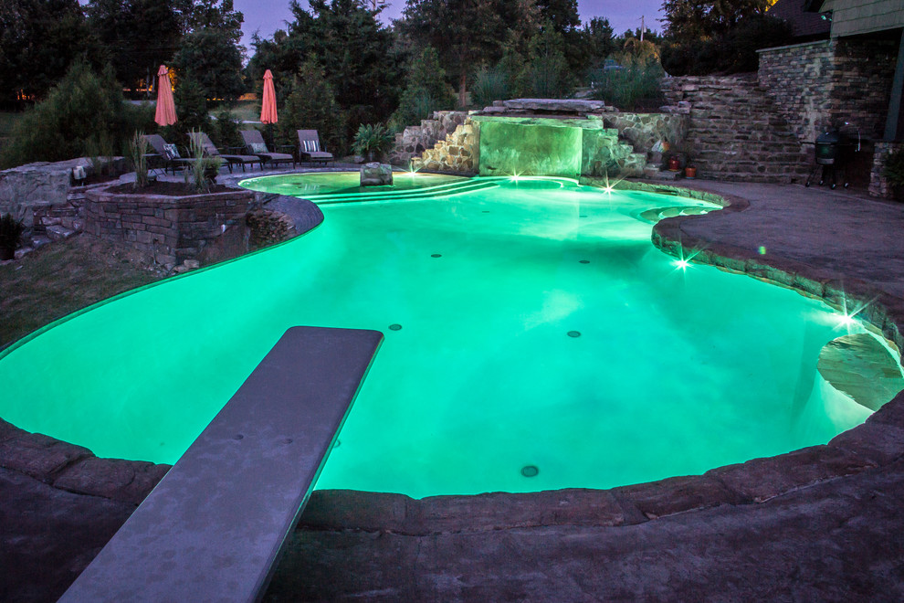 Large world-inspired back custom shaped swimming pool in Chicago with a water feature and stamped concrete.
