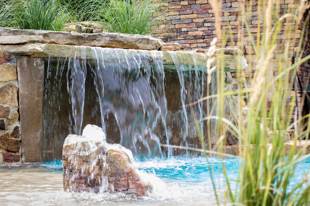 Modelo de piscina con fuente natural exótica grande a medida en patio trasero con suelo de hormigón estampado