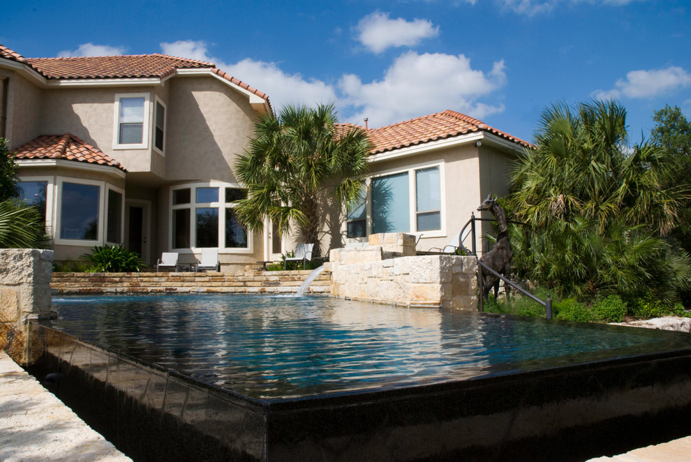 Medelhavsstil inredning av en stor anpassad infinitypool på baksidan av huset, med en fontän och naturstensplattor