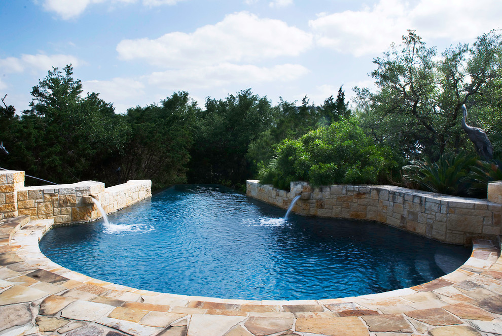 Immagine di una grande piscina a sfioro infinito mediterranea personalizzata dietro casa con fontane e pavimentazioni in pietra naturale